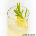 side close up of lavender lemonade cocktail garnished with lavender sprig and lemon wedge