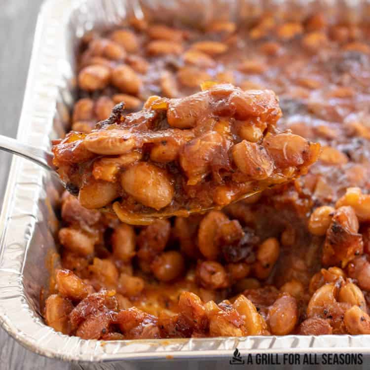 spoon lifting up smoked baked beans from tray
