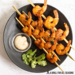 overhead shot of smoked shrimp on skewers on plate with dip and cilantro
