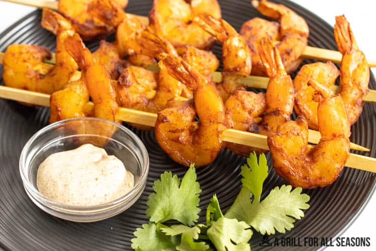smoked shrimp on skewers on plate with dip and cilantro