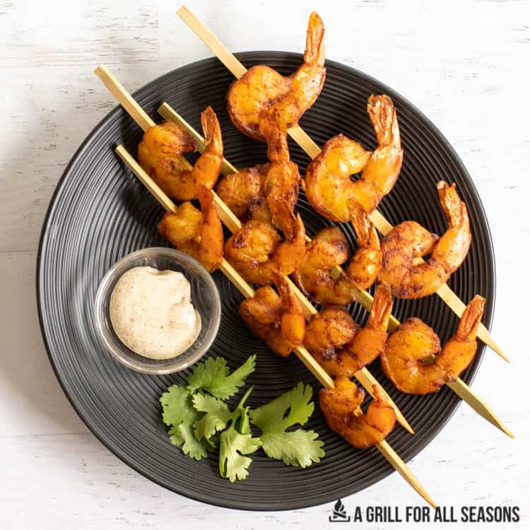 overhead shot of smoked shrimp on skewers on plate with dip and cilantro