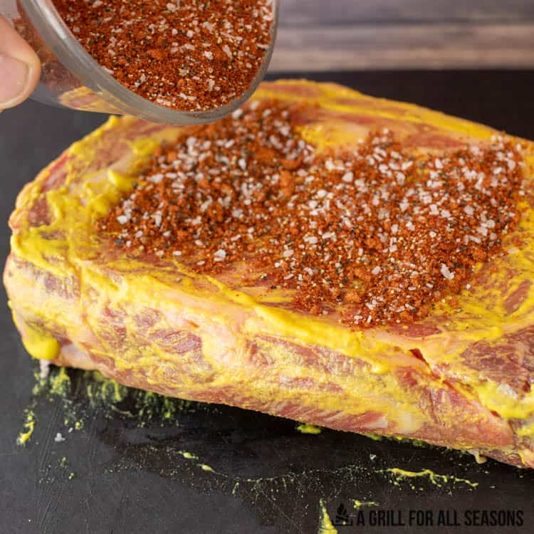 dry rub being poured on steak on top of mustard