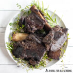overhead shot of smoked beef short ribs on a plate with fresh herbs
