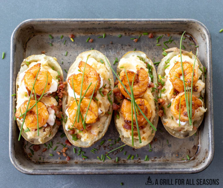 tray of loaded baking potatoes topped with sour cream, bacon, shrimp, and chives