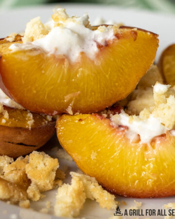 close up of smoked peaches on a plate topped with whipped cream and lemon cookie crumbs