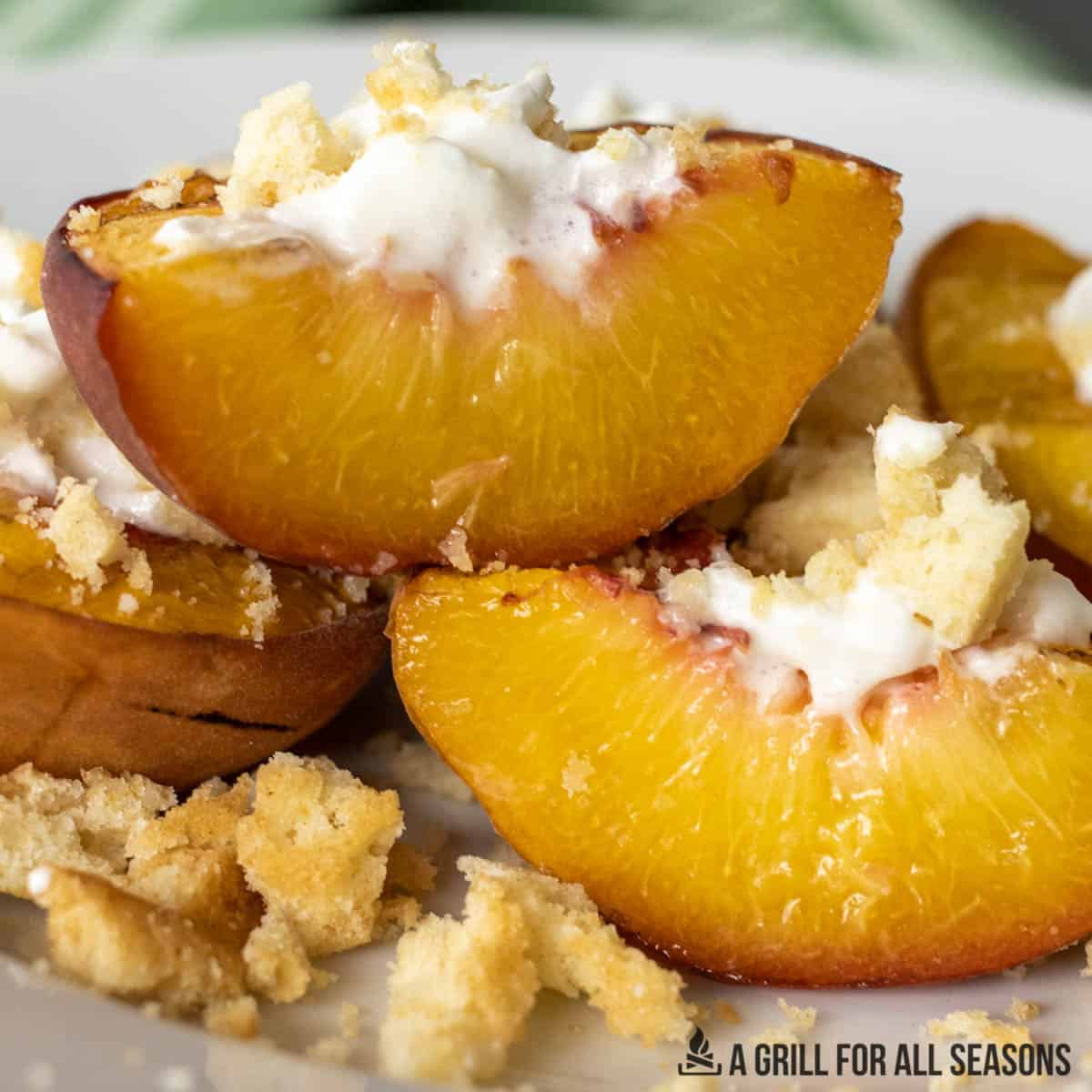 close up of smoked peaches on a plate topped with whipped cream and lemon cookie crumbs