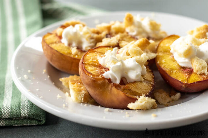 halved smoked peaches on a plate topped with whipped cream and lemon cookie crumbs