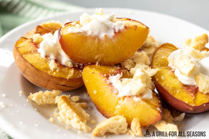 halved and sliced smoked peaches on a plate topped with whipped cream and lemon cookie crumbs