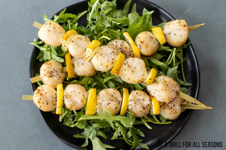 skewers of smoked scallops on bed of arugula on black plate