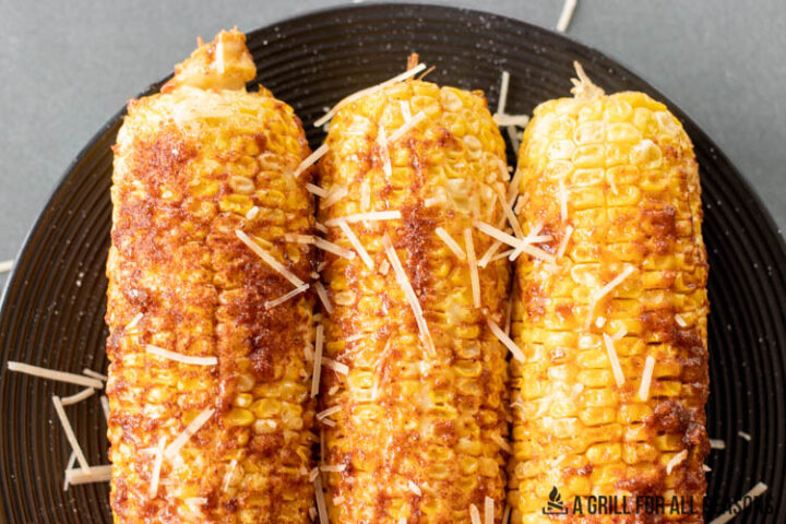 close up of three ears of smoked corn on the cob topped with parmesan cheese and seasoning