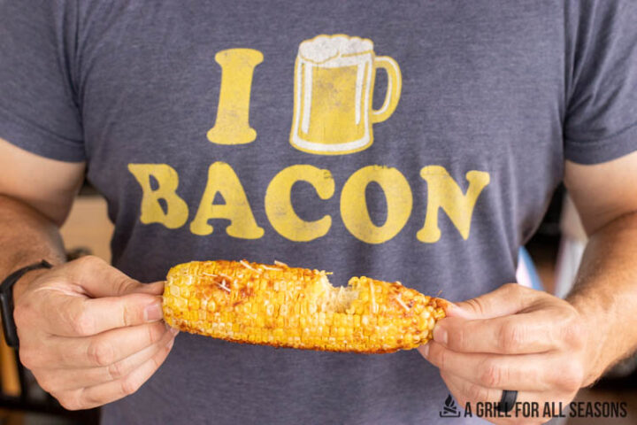 man with i beer bacon shirt on holding ear of corn missing a bite