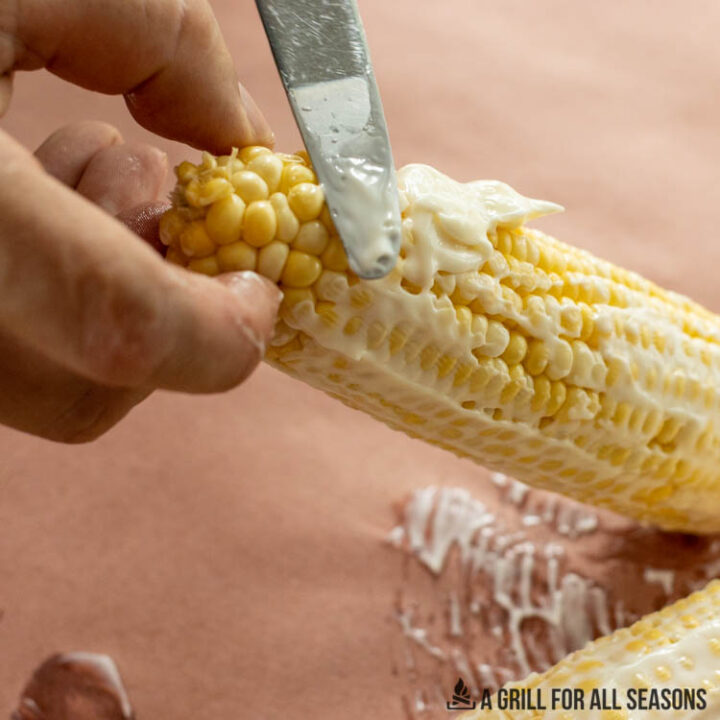 hands spreading mayo on corn with butter knife
