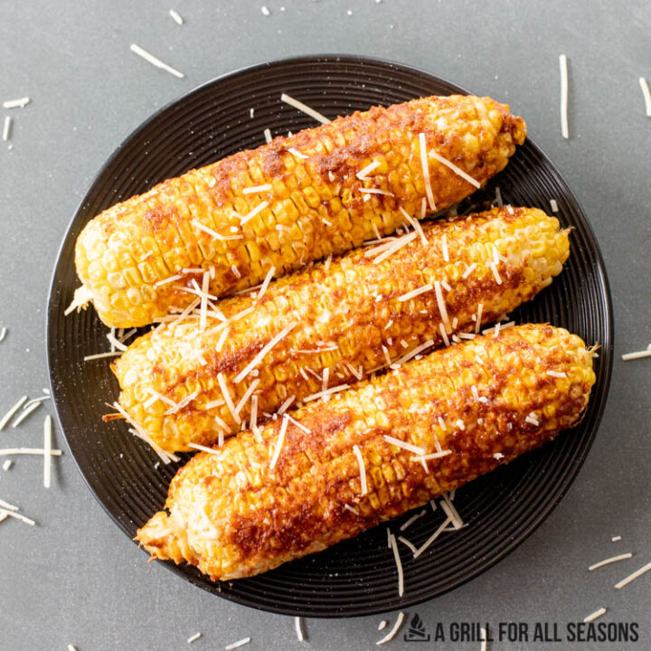 plate with three ears of traeger corn on the cob topped with parmesan cheese and seasoning