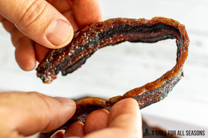 hands bending a piece of bacon jerky to show pliability