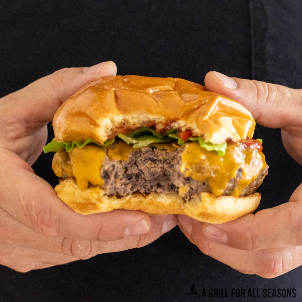 hands holding a wagyu beef burger with a bite missing