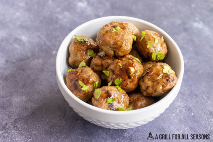 bowl of asian pork meatballs topped with herbs