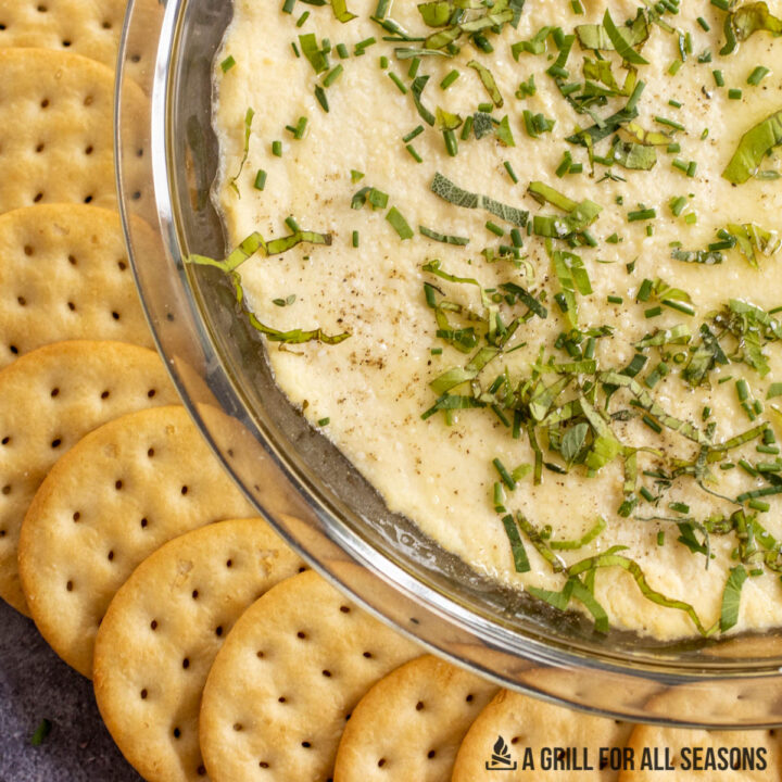 smoked ricotta topped with olive oil and fresh herbs with crackers around it