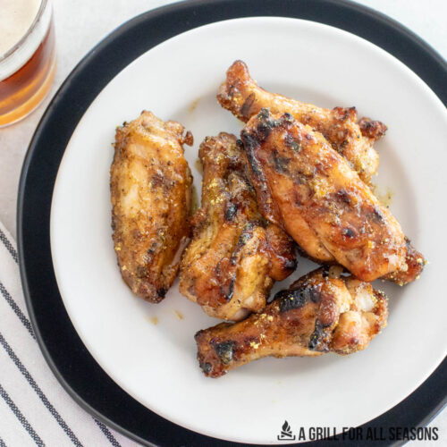 hot honey lemon pepper wings on a white plate with a glass of beer to the side