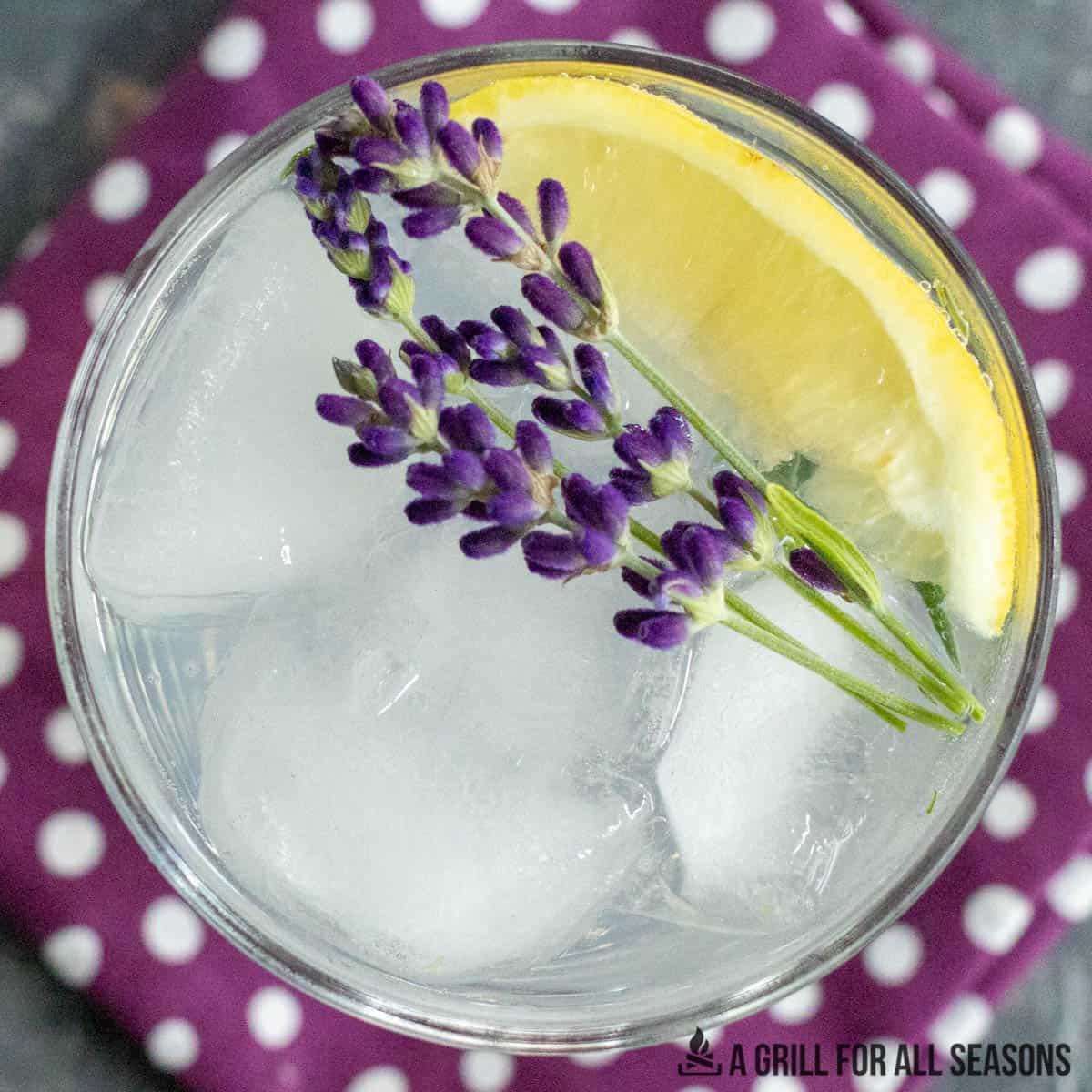 close up overhead shot of a lavender lemonade cocktail garnished with flowers and lemon wedge