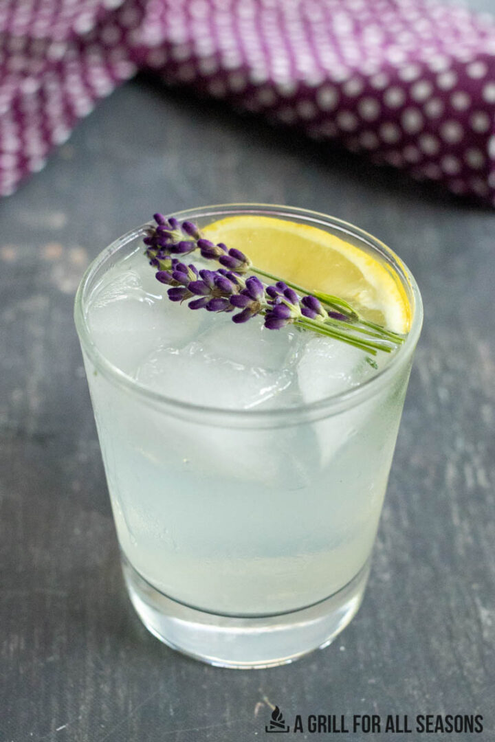 lavender lemonade cocktail garnished with flowers and lemon wedge