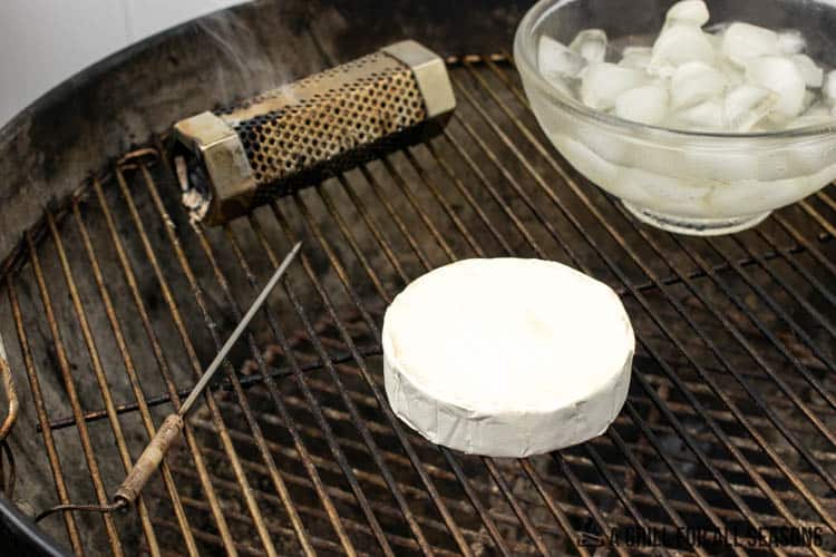 wheel of brie on a grill next to smoking tube and bowl of ice