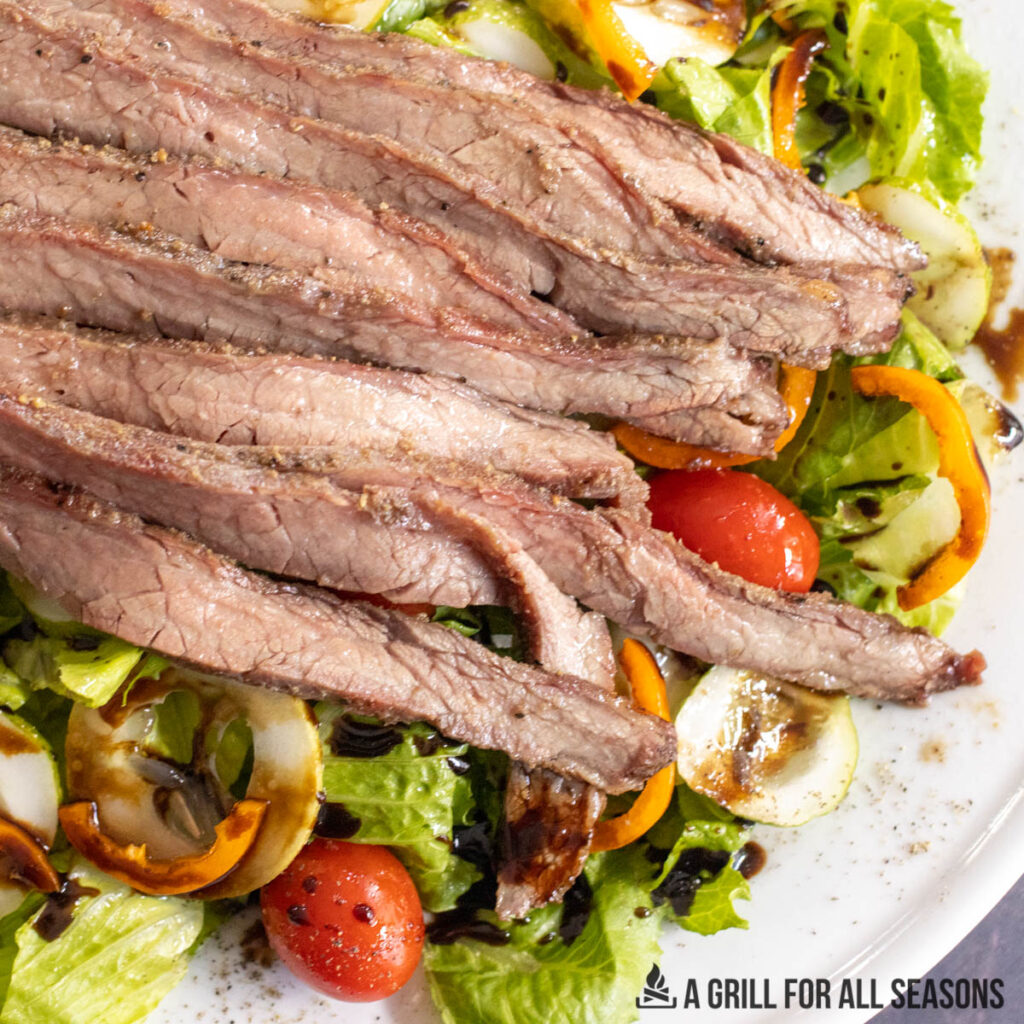 close up of smoked flank steak sliced on top of a garden salad