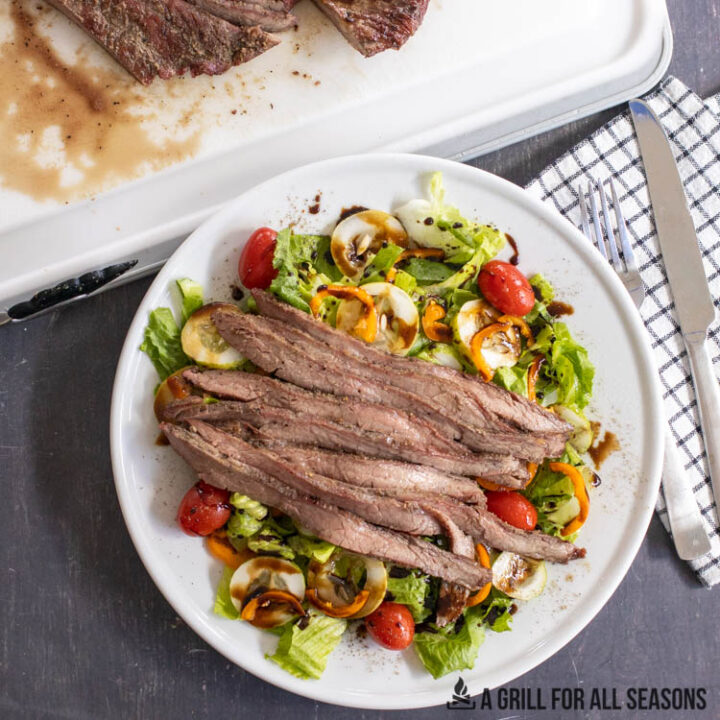 smoked flank steak sliced on top of a garden salad