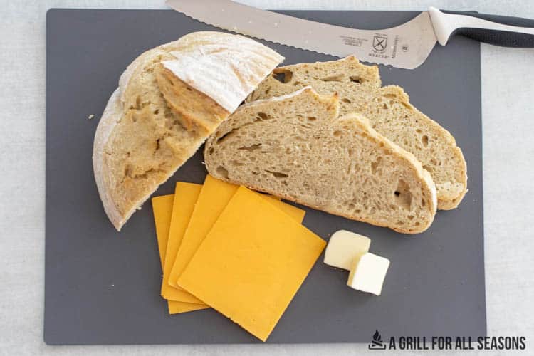 cutting board with sourdough bread, butter, and slices of cheese