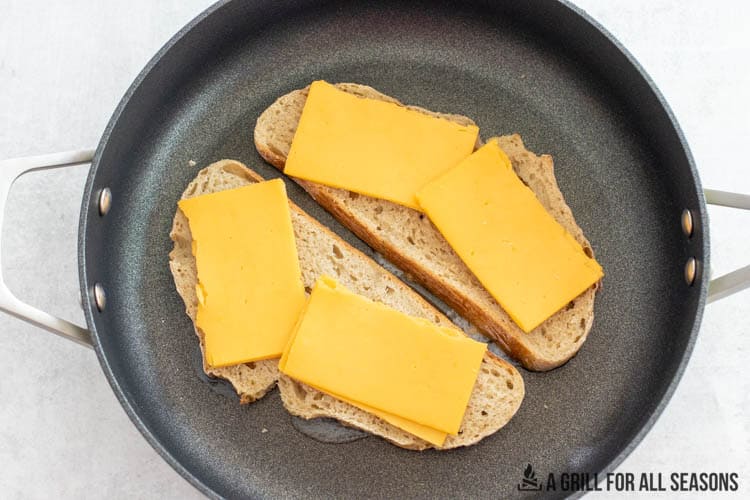 two pieces of sourdough bread in a skillet topped with cheddar cheese