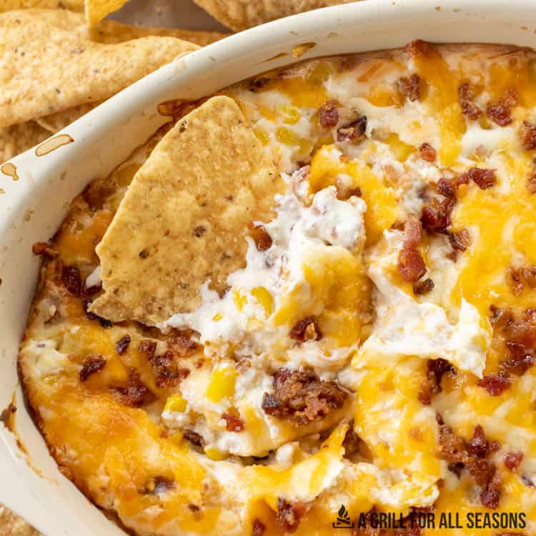 close up of corn dip with cream cheese and bacon with a tortilla chip dipped into it