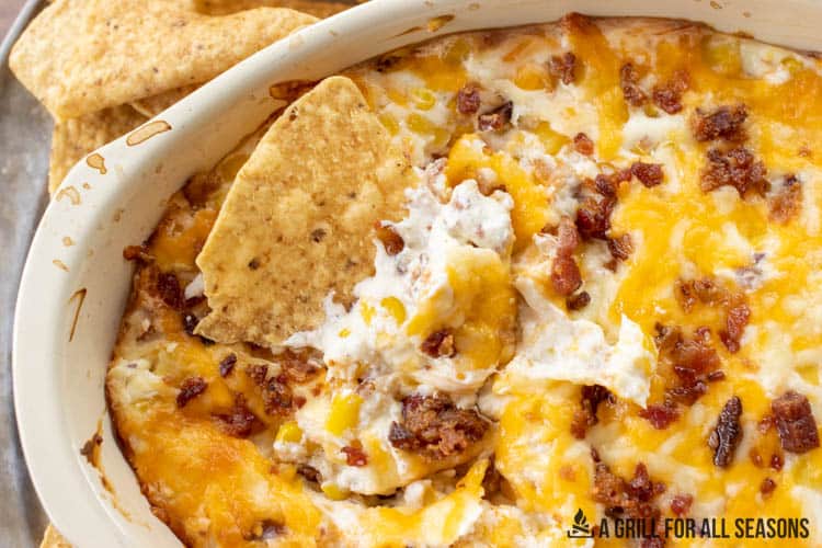 corn dip with cream cheese and bacon with a tortilla chip dipped into it