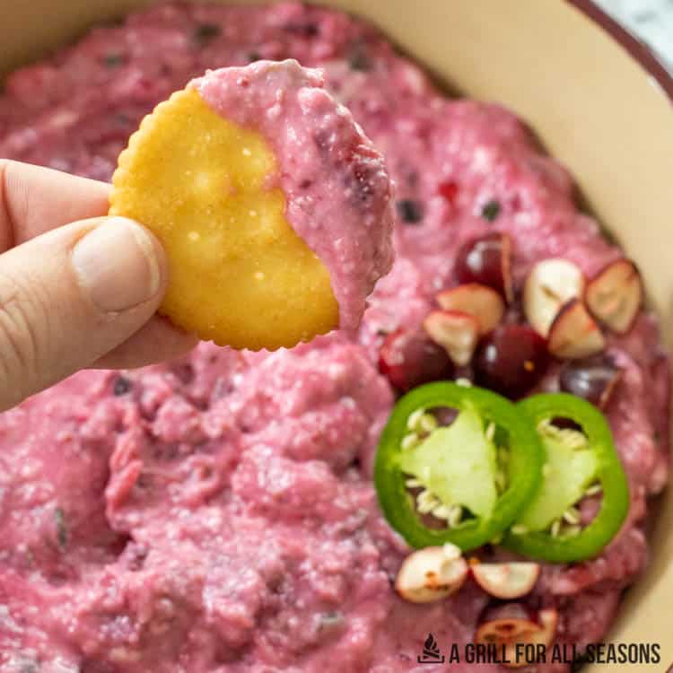 hand lifting up some of the cranberry jalapeno dip on a cracker