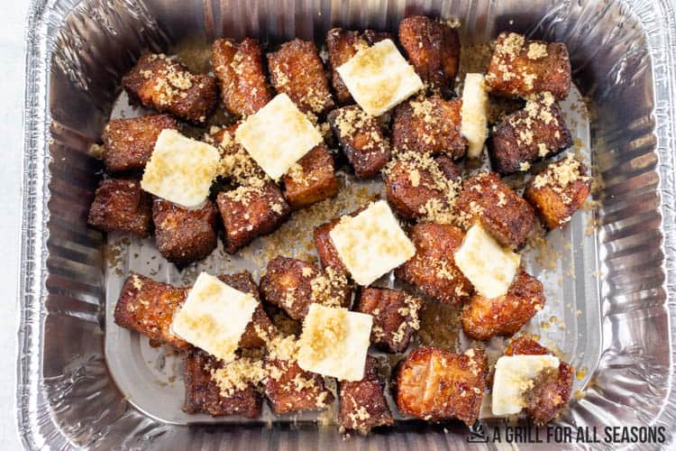 metal pan with pork belly cubes topped with pats of butter and brown sugar