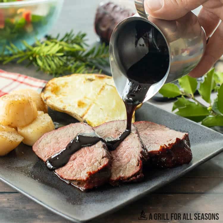 red wine reduction sauce being poured over slices of smoked beef tenderloin