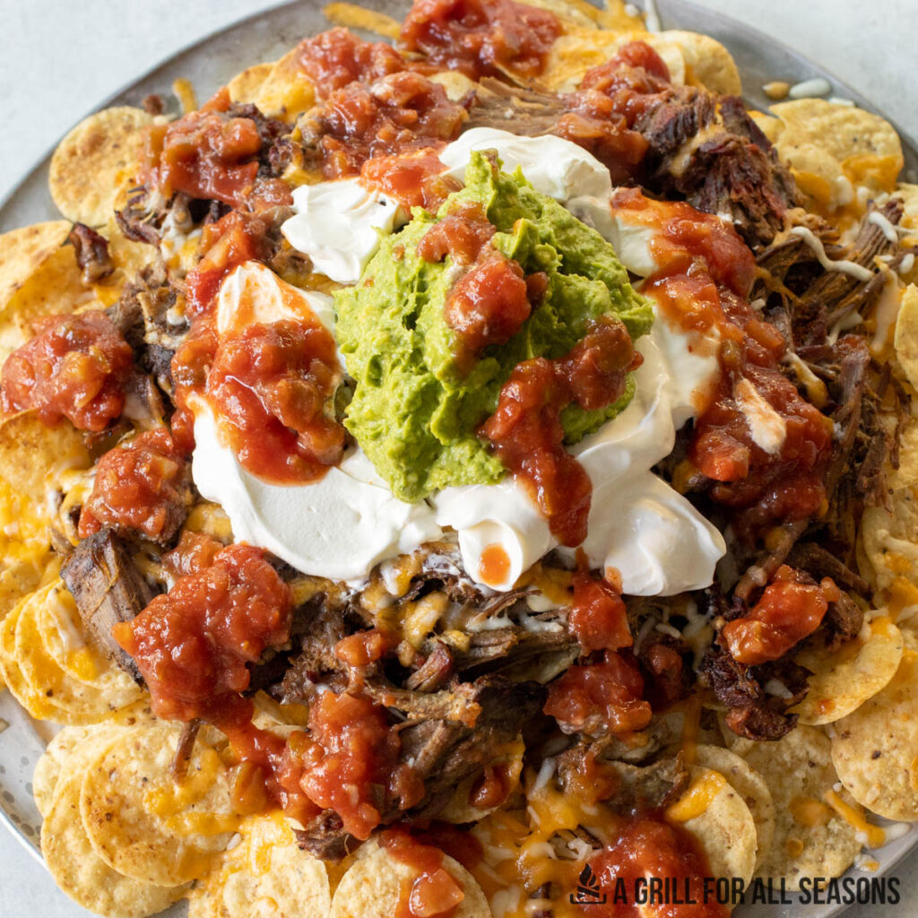 smoked nachos on platter topped with sour cream, salsa, and guacamole