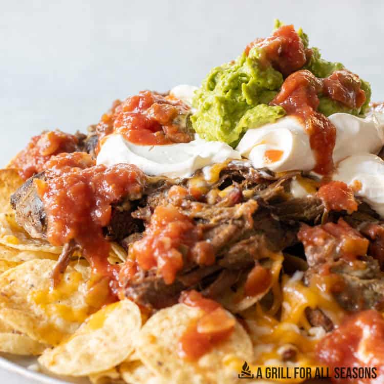 close up of smoked nachos on platter topped with sour cream, salsa, and guacamole