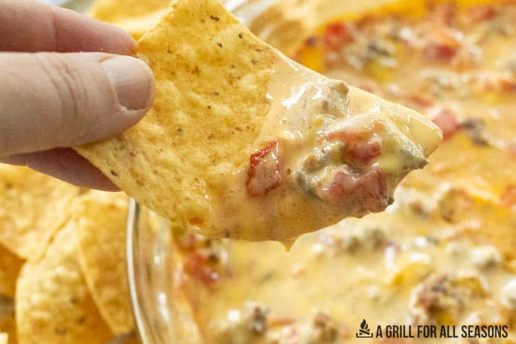 hand holding tortilla scooping up dip from the smoked queso recipe