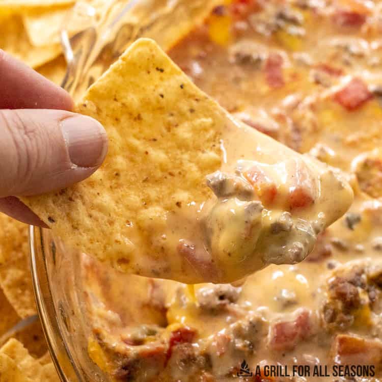 hand holding tortilla scooping up dip from the smoked queso recipe