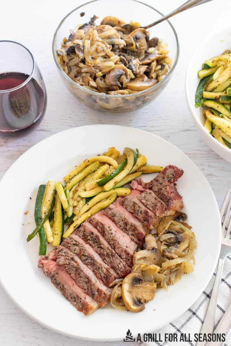 plated steak with sides in bowls and glass of wine