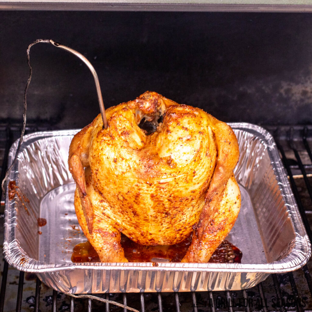 traeger beer can chicken on the traeger pellet grill in an aluminum pan with thermometer probe