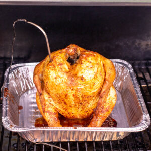 traeger beer can chicken on the traeger pellet grill in an aluminum pan with thermometer probe
