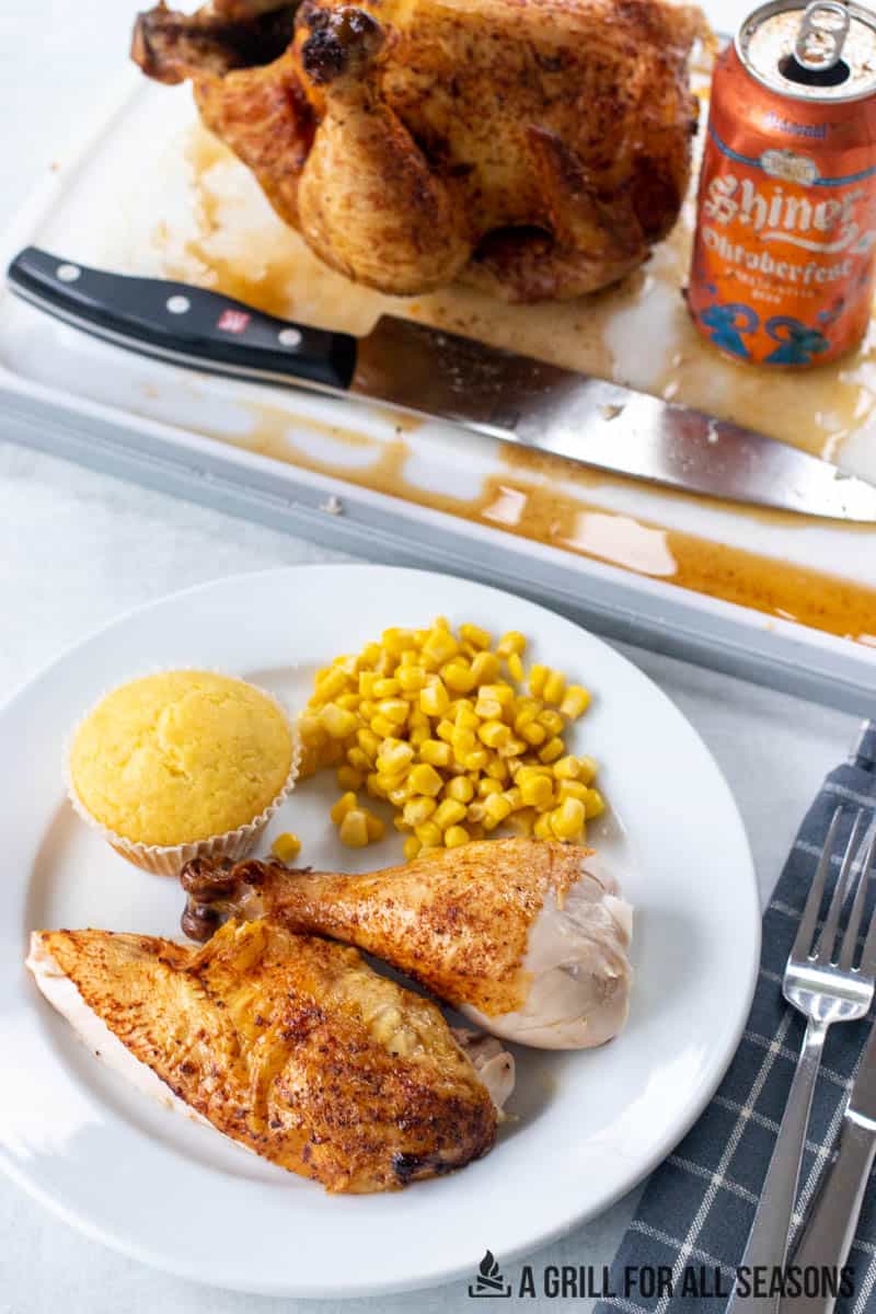 traeger beer can chicken pieces on a plate with cutting board of whole chicken behind next to beer can