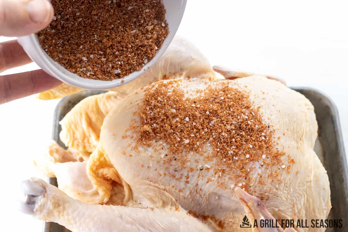 dry rub being sprinkled on whole chicken