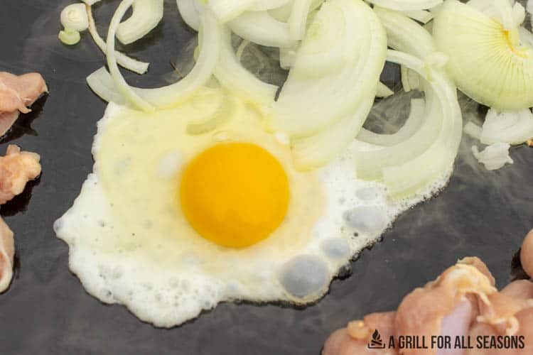 egg being cooked on blackstone with other ingredients in background