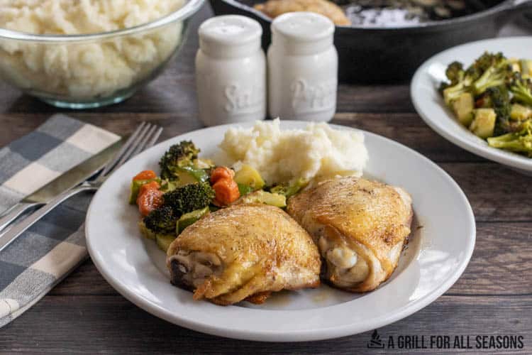 cast iron chicken on plate with vegetables and potatoes with table set behind