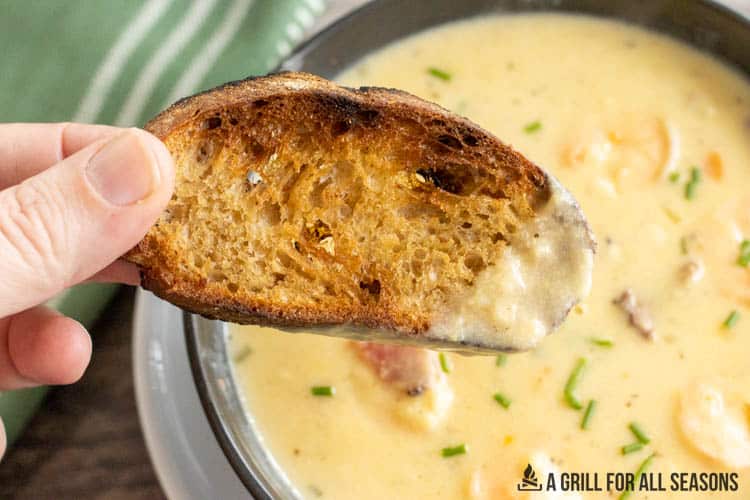 hand holding up bread dipped in the shrimp and corn bisque