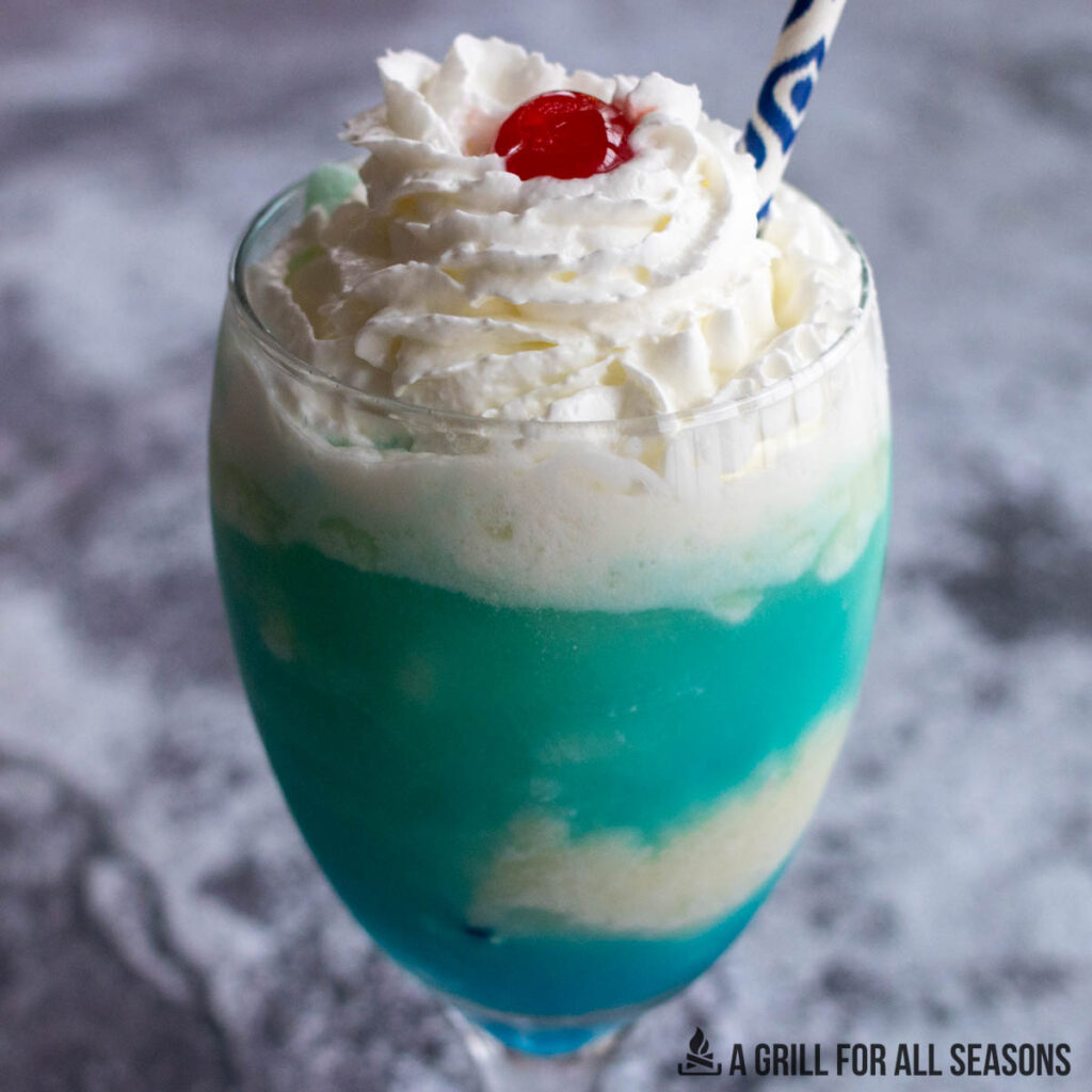 blue colada in a stemmed glass with a straw and cherry