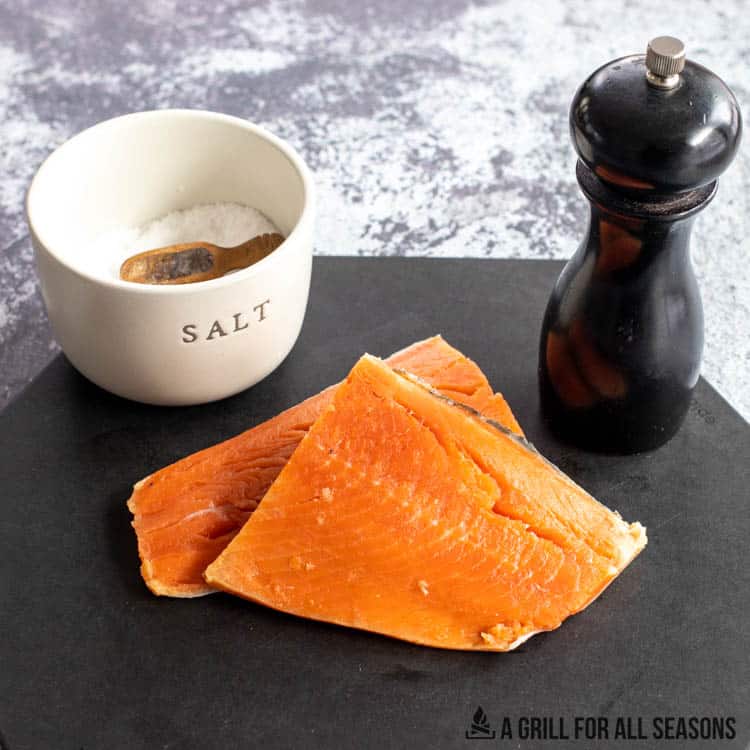 salmon filets on cutting board with bowl of salt and pepper mill