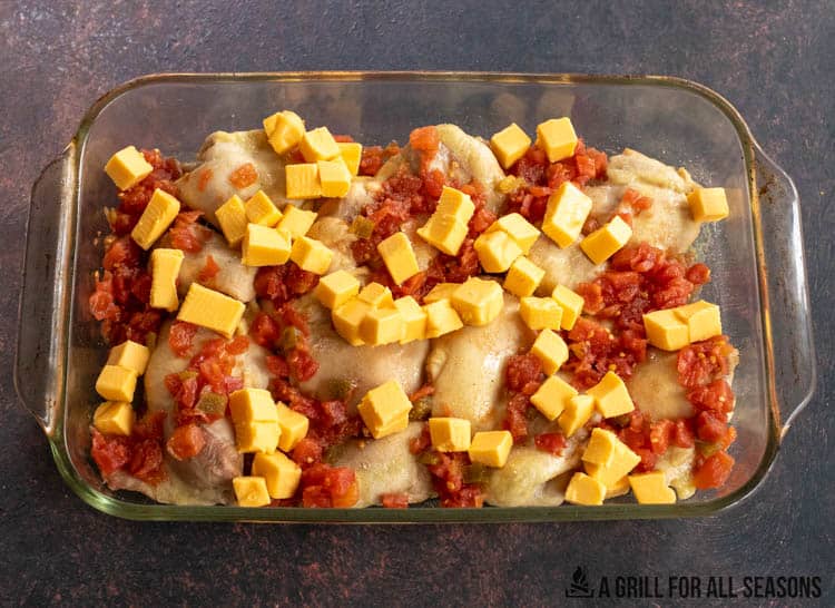 cooked chicken thighs in casserole dish covered with cubed cheese and rotel