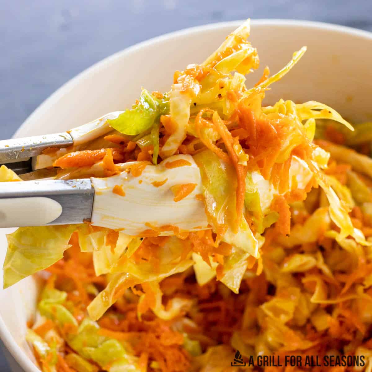 tongs lifting cabbage and carrot salad